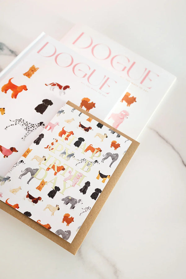 Birthday card illustrated with colorful dogs and gold foil “Happy Birthday” text, placed on a kraft envelope.