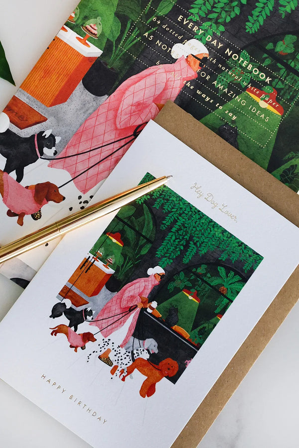 Colorful notebook and greeting card set with dog illustrations and green botanical background, styled with coffee and gold pen — All the Ways to Say stationery.