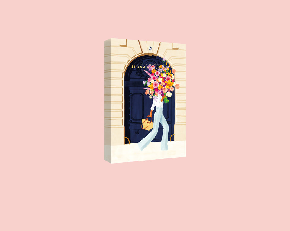 Hand-painted illustration of a stylish woman with a blooming flower bouquet head walking through a Parisian doorway on a 1000-piece jigsaw puzzle box.