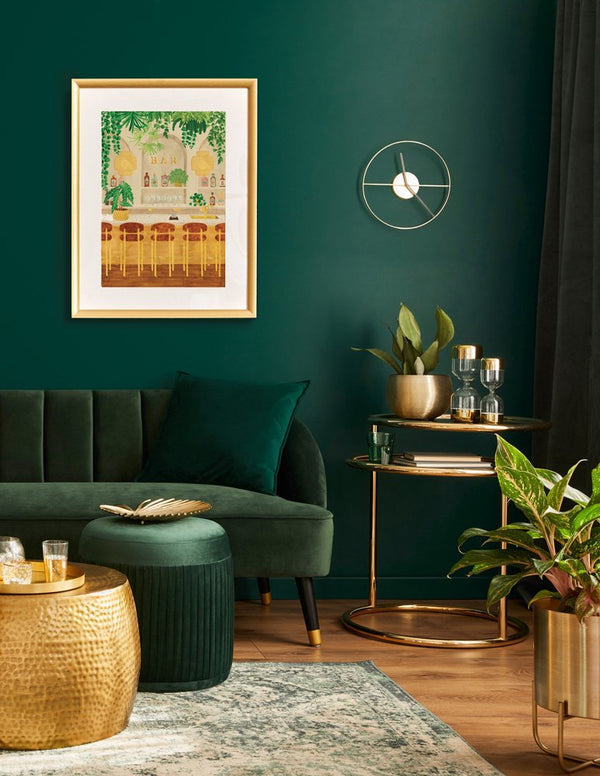 Gold framed Bar poster displayed on a dark green wall above a luxury velvet sofa with gold decor accents.
