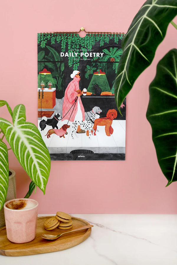 Daily Poetry 2026 calendar by All The Ways To Say hanging on pink wall with plants and coffee cup
