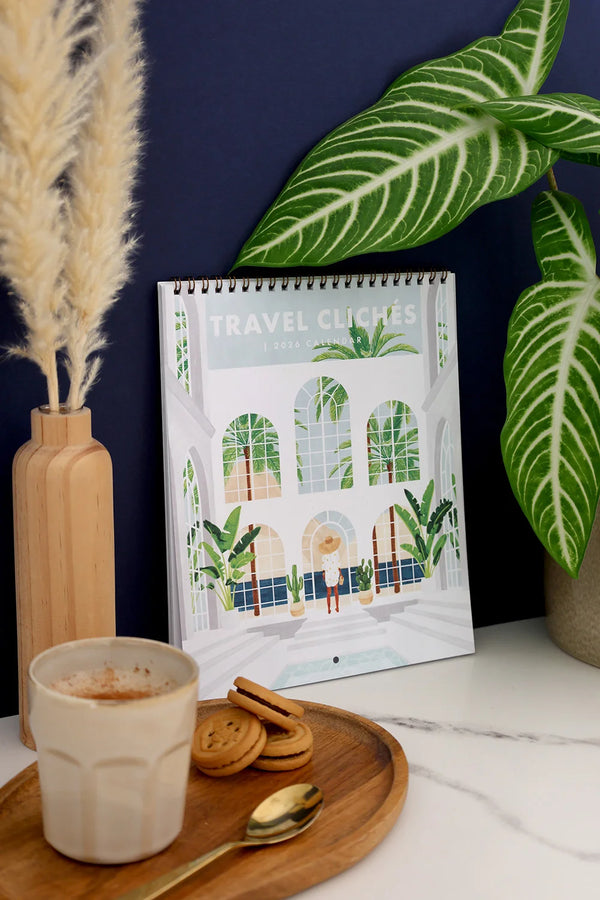 Close-up of Travel Clichés 2026 calendar cover – woman standing in tropical glasshouse illustration