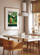 Framed Chic Watering poster hanging in a bright, modern dining room with rattan chairs and a white tiled table.