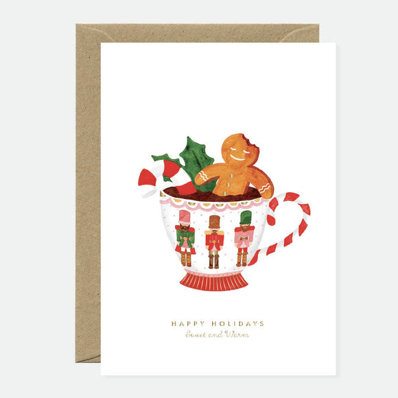 Greeting card with a Christmas theme, featuring an illustration of a gingerbread man in a cup with holiday decorations, and text that reads 'Happy Holidays'.