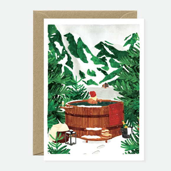 A greeting card with an illustration of a wooden hot tub in a snowy forest setting, accompanied by a recycled brown envelope.