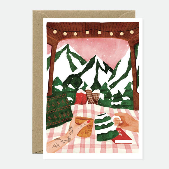Illustration of two hands holding mugs on a checkered blanket, with snowy mountains, pine trees, and a wooden canopy in the background.