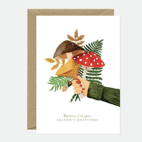 Greeting card with an illustration of a bouquet of mushrooms and greenery, with gold foil accents, held by a hand. The card has a blank interior and comes with a recycled brown envelope.