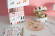 Dog print accessories collection with card holder, jewelry case, and Dogue notebook styled on marble desk with gold jewelry.