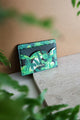 Green Cliff card holder displayed on a stone surface with tropical leaves in the background, elegant botanical pattern by All the Ways to Say.