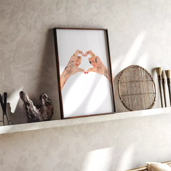 Framed Hands of love poster leaning on a floating ledge alongside artistic paintbrushes and a round woven tray.
