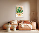 Inside out house poster displayed in a wooden poster hanger on a beige wall above a brown leather sofa with textured cushions.