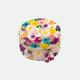 A round jewellery box with a floral pattern in shades of pink, yellow, and green, closed with a gold-colored zipper.