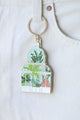 Close-up of Green House enamel keychain by All The Ways To Say – glasshouse with tropical plants illustration