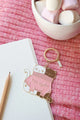 2 Cats in a Sweater keychain by All The Ways To Say placed on pink blanket with marshmallows and notebook