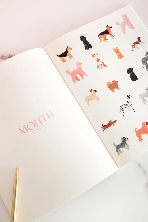 Inside view of the Dogue monthly planner featuring watercolor dog illustrations and pink “Month by Month” title on a clean white page.