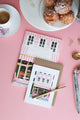 Close-up of pink bakery notebook cover with striped awning and golden details — eco-friendly stationery by All the Ways to Say.