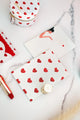 Notebook with red heart pattern on white cover styled with lipstick, pouch, and accessories on marble surface.
