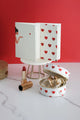Romantic notebook with red heart design on white cover, displayed with jewelry case and lipstick against red background.