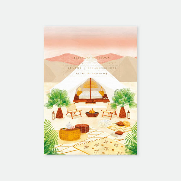 A5 notebook with a gold foil cover featuring an illustration of a desert scene with a tent, palm trees, and campsite furniture.