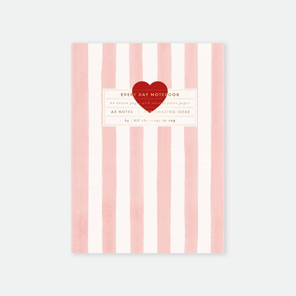 A5 sized notebook with pink and white stripes and gold foil details, featuring a heart emblem and text on the cover.