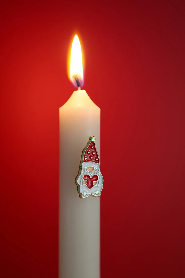 Close-up of Grumpy Heart enamel pin by All The Ways To Say – gnome with red hat and heart on white candle, holiday background