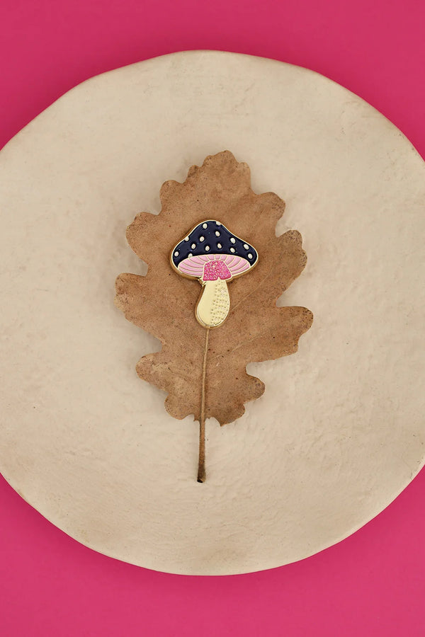 Crazy Mushroom enamel pin by All The Ways To Say on brown oak leaf over beige plate – pink background