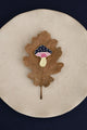 Crazy Mushroom enamel pin by All The Ways To Say on oak leaf over beige plate – navy blue background, minimal fall style