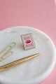Bisou Bella enamel pin by All The Ways To Say on marble tray with gold pen and paper clips – pink background lifestyle photo