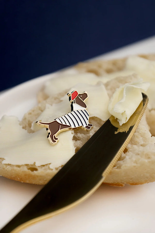 Close-up of Little Frenchie enamel pin by All The Ways To Say – dachshund dog in striped shirt and red beret on bread background