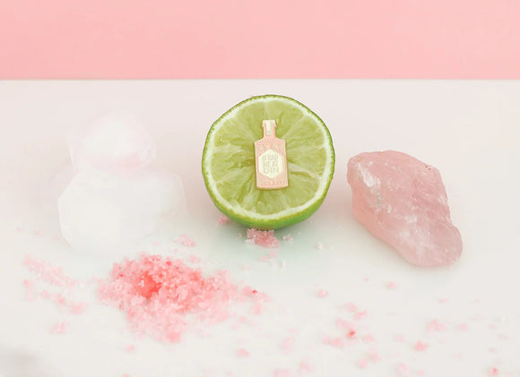 Pink gin bottle enamel pin displayed on a lime half with ice cubes, pink sugar, and rose quartz stone