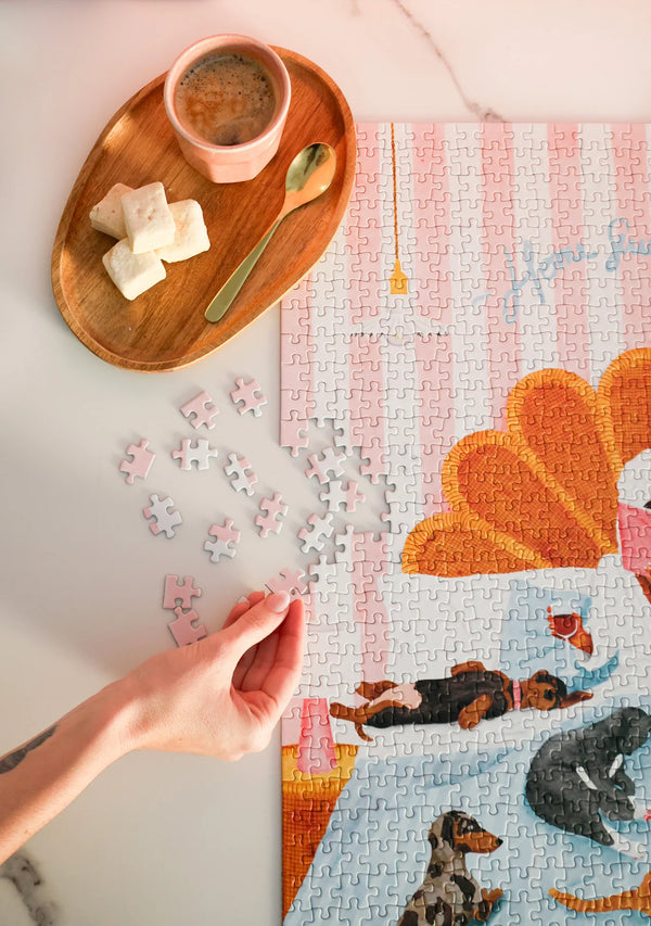 Hand placing a piece of the Home Sweet Home puzzle – soft pink and blue tones