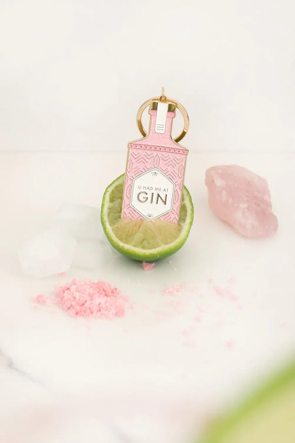 Pink glitter gin bottle keychain resting inside a cut lime with pink salt and ice blocks.