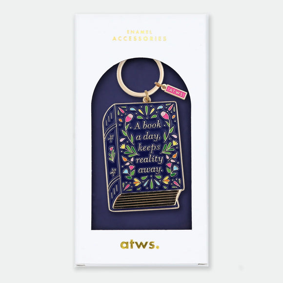 Enamel and metal keychain shaped like a navy storybook covered in colorful flowers, text reading "A book a day, keeps reality away," gold-tone ring and "ATWS" charm