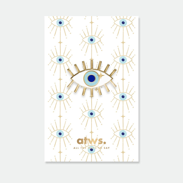 A radiant blue lucky eye enamel pin by All The Ways To Say with gold rays, displayed on a matching patterned backing card.