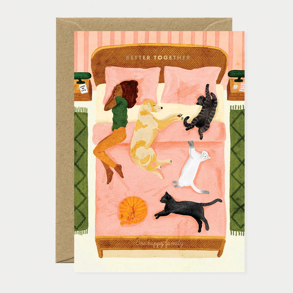 A cozy watercolor greeting card by All The Ways To Say showing a person and five pets (dog and cats) sharing a bed with the text "BETTER TOGETHER".