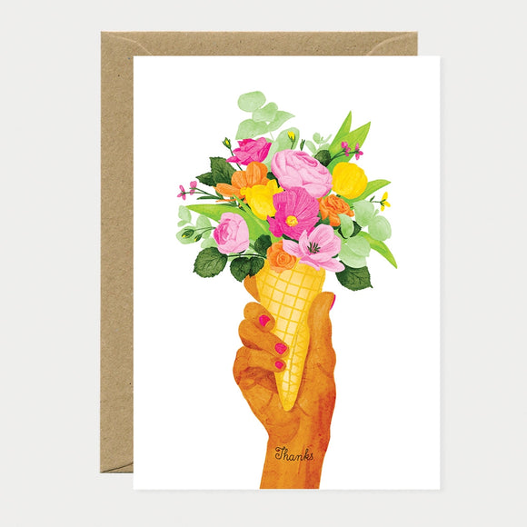 A whimsical greeting card by All The Ways To Say featuring a watercolor hand holding a waffle cone filled with a colorful bouquet of flowers and the word "Thanks" on the wrist.