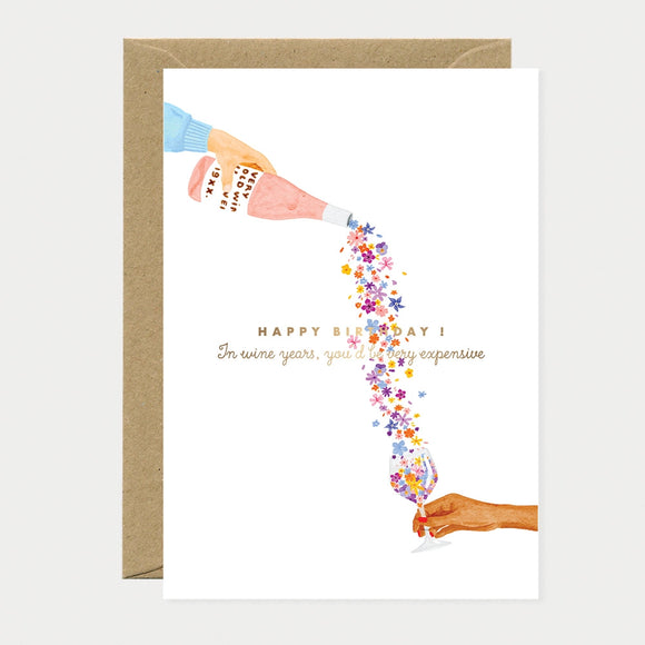 A poetic watercolor greeting card by All The Ways To Say showing a hand pouring a stream of flowers from a wine bottle into a glass with a birthday message.