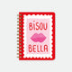 A large red spiral notebook by All The Ways To Say featuring a pink stamp with lips, the text "BISOU BELLA", and gold foil details.