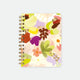 A large spiral notebook by All The Ways To Say featuring a colorful watercolor floral pattern and gold foil details on the cover.