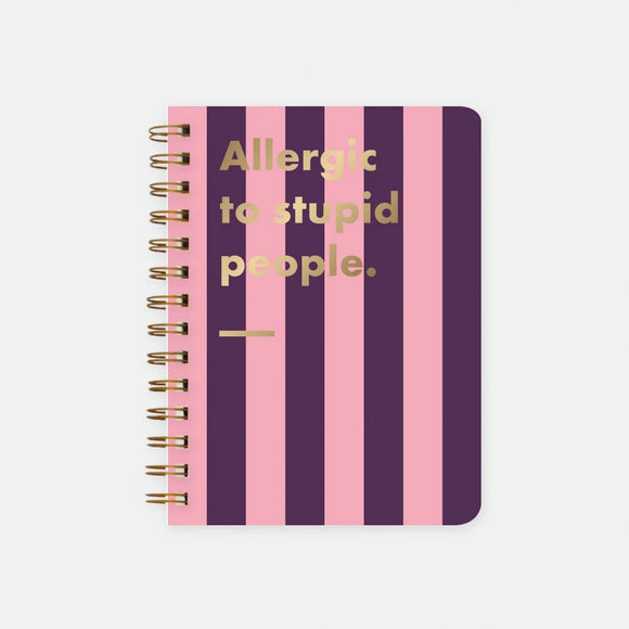 Allergic To Stupid People A5 spiral notebook by All The Ways To Say, bold purple and pink striped cover with "Allergic to stupid people." text in gold foil lettering and a gold underline, spiral binding visible on the left edge