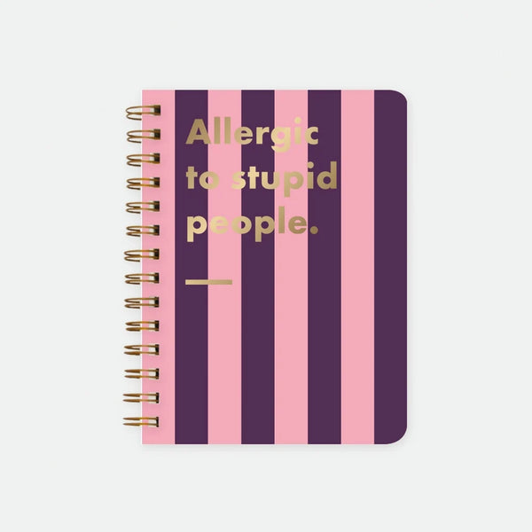 Allergic To Stupid People A5 spiral notebook by All The Ways To Say, bold purple and pink striped cover with "Allergic to stupid people." text in gold foil lettering and a gold underline, spiral binding visible on the left edge