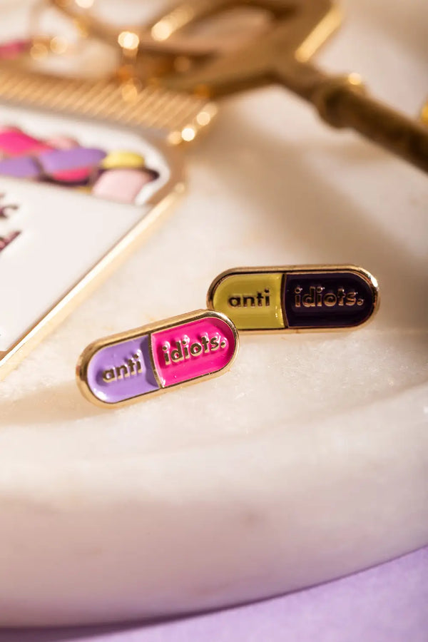 Duo Anti Idiots - Pins: a set of two colorful enamel pins shaped like medical capsules.