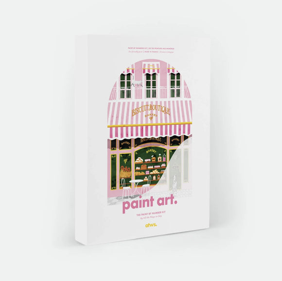 Bakery paint by numbers kit box by All The Ways To Say, illustration of a pink and white striped "Biscuit Boutique" bakery storefront with pastries in the window, a white cat on the balcony above and a Dalmatian outside on the pavement, "paint art. The Paint By Number Kit by All The Ways To Say"