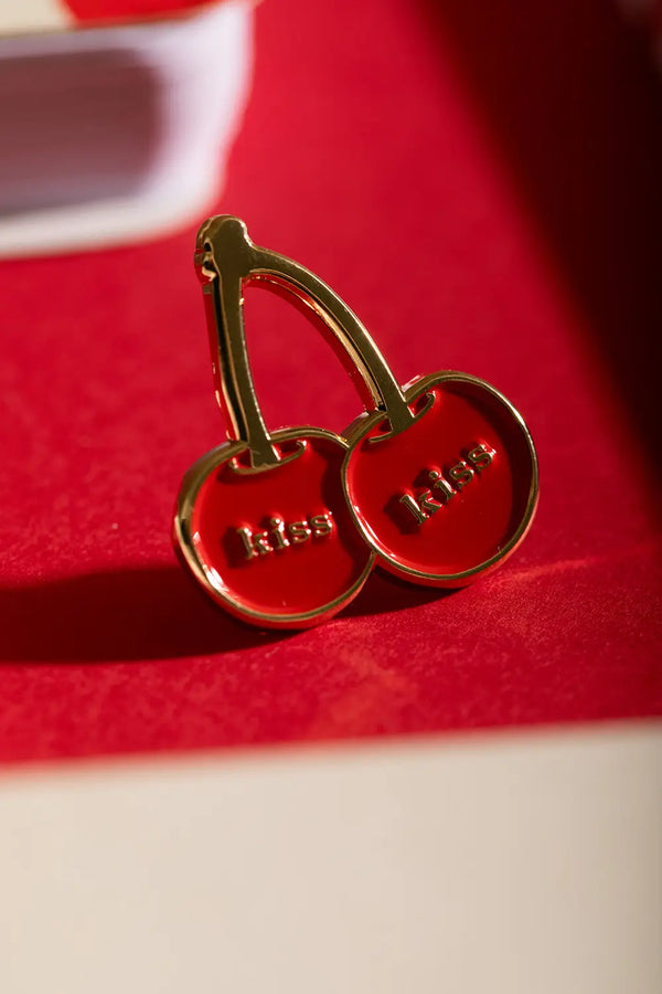 Kiss Kiss - Pins: close-up of the cherry pin highlighting the shiny gold plating and vibrant red enamel.