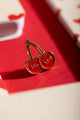 Kiss Kiss - Pins: a red cherry-shaped enamel pin with the word "Kiss" embossed on each cherry.