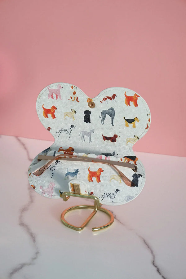 Open glasses case with colorful dog illustrations, displayed on a gold stand.