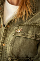Dachshund shark enamel pin worn on the chest pocket of an olive denim jacket over a white t-shirt
