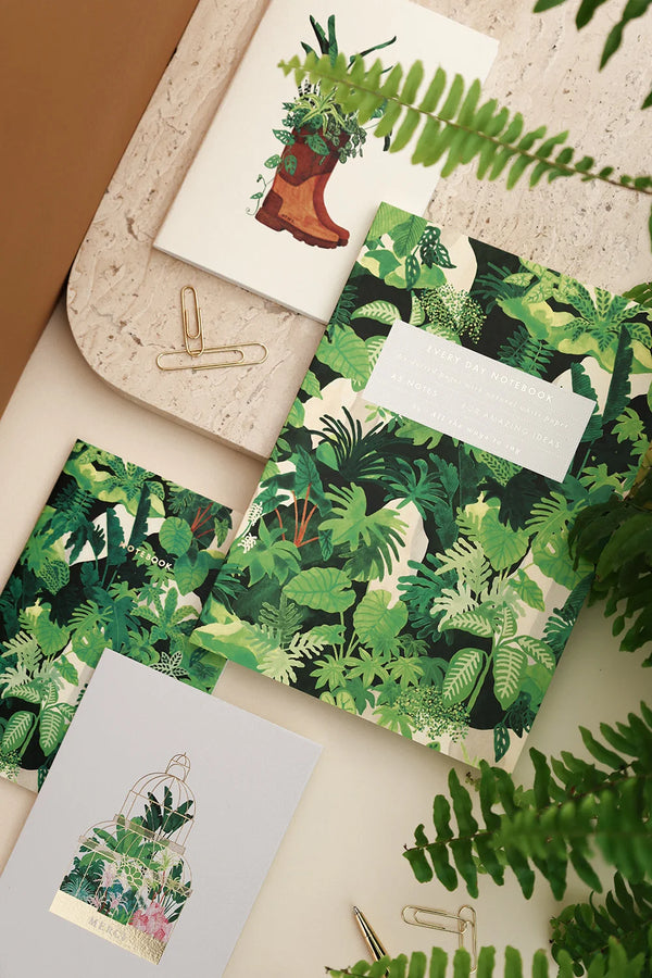 Green Cliff botanical notebooks and stationery with lush jungle leaf patterns, surrounded by ferns.