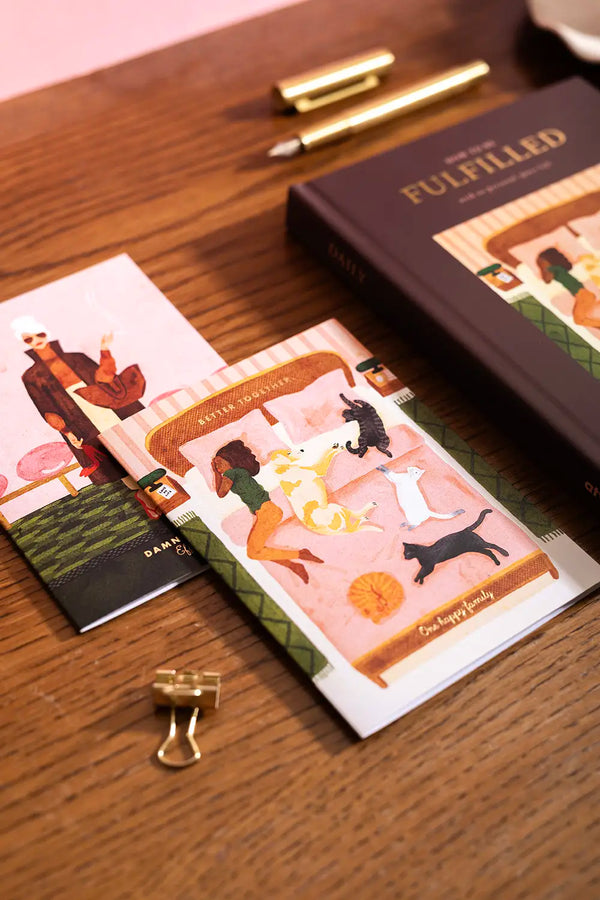 Happy pets Greeting card - Cozy lifestyle illustration featuring dogs and cats on a bed, displayed on a wooden table.