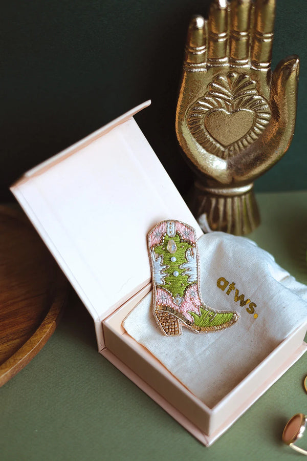 Hand-embroidered cowboy boot brooch in pink and lime green silk threads with gold beads, displayed in a light pink gift box.